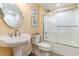 A well-lit bathroom with a pedestal sink, round mirror, and shower-tub combo featuring a glass door at 233 Banbury Ln. # 302, Little River, SC 29566