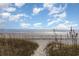 Sandy beach with distant waves is framed by dunes and a beautiful blue sky at 105 S Ocean Blvd. # 108, North Myrtle Beach, SC 29582