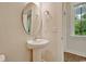 Bright half-bathroom featuring a pedestal sink, oval mirror, and natural light from a window at 67 Bridgeview Rd., Georgetown, SC 29440