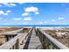 Scenic wooden walkway leads to a sandy beach and blue ocean, perfect for a relaxing coastal getaway at 1582 S Waccamaw Dr. # 44, Murrells Inlet, SC 29576