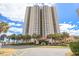 High-rise condo building boasts lush landscaping with tropical palm trees along a scenic road near the beach at 8560 Queensway Blvd. # 1206, Myrtle Beach, SC 29572