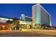 Illuminated hotel complex with pedestrian bridge over the street and modern architectural design against a twilight sky backdrop at 1501 S Ocean Blvd. # 844, Myrtle Beach, SC 29577