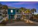 Inviting coastal home featuring a turquoise exterior, white railings, and lush palm trees in the landscaped front yard at 409 25Th Ave. N, North Myrtle Beach, SC 29582