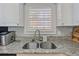 Well-maintained kitchen sink area featuring stainless steel dual basin sink, modern faucet, granite countertops, and white cabinets at 4803 Bovardia Pl. # 102, Myrtle Beach, SC 29577