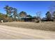 Exterior view of a home with a green metal roof and a covered porch, surrounded by trees and a dirt road at 1264 Harrelson Dr., Longs, SC 29568