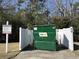 A green waste management dumpster is surrounded by trees and a white fence at 721 Painted Bunting Ct. # C, Murrells Inlet, SC 29576