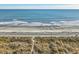 Sandy beach with foamy waves, with tall beach grass dunes in the foreground, under a clear sky at 4616 Greenbriar Dr. # H8, Little River, SC 29566