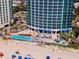 Aerial view of pool area with lounge chairs and umbrellas by a sandy beach area at 107 S Ocean Blvd. # 704, Myrtle Beach, SC 29577