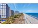 Breathtaking view of sandy beach with high-rise buildings, beachgoers, and blue umbrellas, offering a perfect coastal escape at 5308 N Ocean Blvd. # 503, Myrtle Beach, SC 29577