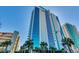 Modern high-rise condo building with blue glass and white accents, surrounded by lush palm trees and greenery at 107 S Ocean Blvd. # 1407, Myrtle Beach, SC 29577