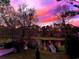 Scenic backyard view featuring a tranquil pond, a wooden shed and a vibrant pink and purple sunset sky at 532 Medcalf Dr. Sw, Sunset Beach, NC 28468