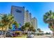 Beautiful exterior view of Carolina Winds with swaying palm trees on a bright, sunny day at 200 76Th Ave. N # 1211, Myrtle Beach, SC 29572