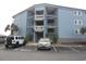Three story blue condo building showing the parking area with tropical plants at 9540 Shore Dr. # 3-H, Myrtle Beach, SC 29572