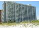 Beautiful exterior of a tall building with many balconies and a view of beach and grassy dunes at 9820 Queensway Blvd. # 607, Myrtle Beach, SC 29572
