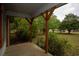 A covered porch with weathered support beams and red trim, overlooks a spacious, grassy yard with mature trees at 1001 Creel St., Conway, SC 29527
