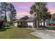 Single-story home with a well-manicured lawn and driveway, enhanced by mature trees on a partially clouded sky at 174 Sussex Ct., Longs, SC 29568