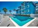 Community pool with clear blue water and palm trees behind blue condo building at 720 N Waccamaw Dr. # 207, Garden City Beach, SC 29576