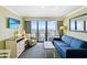 A well lit living room with blue furniture, TV, and ocean view balcony at 3000 N Ocean Blvd. # 729, Myrtle Beach, SC 29577