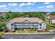 Aerial view of a condo building featuring a well-manicured lawn and ample parking surrounded by lush trees under a blue sky at 5750 Oyster Catcher Dr. # 1135, North Myrtle Beach, SC 29582