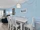 A bright dining area with light blue walls, white table and chairs, decorative light, and view into the living room at 5000 N Ocean Blvd. # B-1, North Myrtle Beach, SC 29582