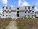 Rear exterior shot of a gray condominium building with multiple decks accessible from a grassy path from the beach at 5000 N Ocean Blvd. # B-1, North Myrtle Beach, SC 29582