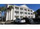 Exterior view of condo building with white siding, columned balconies, palm trees, and parking spaces at 5020 Windsor Green Way # 302, Myrtle Beach, SC 29579