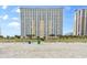 View of the oceanfront condo building from the beach with a sandy shore, palms, and blue sky overhead at 2000 N Ocean Blvd. # 502, Myrtle Beach, SC 29577