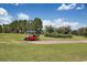 Bright red golf cart near a golf course, surrounded by green grass and trees with a cloudy sky at 977 Cherrystone Loop, Conway, SC 29526