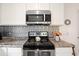 Close-up of a modern stove with stainless steel microwave and patterned tile backsplash at 175 Cypress Ln., Little River, SC 29566