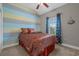 A cozy bedroom with a patterned bedspread, colorful striped accent wall and ceiling fan at 713 Garland Ct., Myrtle Beach, SC 29588