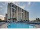 Beautiful exterior shot of a high-rise building with a pool, chairs, and tables at 9820 Queensway Blvd. # 704, Myrtle Beach, SC 29572