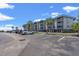 Seaside condo building with a gray facade, blue roof, and palm trees against a partly cloudy blue sky at 6001 N Ocean Blvd. # 147, North Myrtle Beach, SC 29582