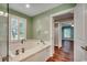 A bathroom with a large bathtub, wood-look flooring, a window, and an open doorway to the bedroom at 107 Azalea Dr., Conway, SC 29526