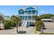 Charming blue beach house with double balconies and white stairs, surrounded by lush landscaping at 4206 S Ocean Blvd., North Myrtle Beach, SC 29582