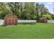 Spacious backyard with two wooden sheds, a white fence, green grass, and a fire pit at 210 Fox Hunt Pl., Aynor, SC 29511