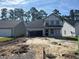 New construction home with a two-car garage surrounded by dirt and other homes in the distance at 402 Sun Colony Blvd., Longs, SC 29568
