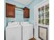 Well-lit laundry room with blue walls, washer, dryer and wooden cabinets above appliances at 6357 Highway 707, Myrtle Beach, SC 29588