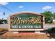 Entrance sign for River Hills Golf & Country Club, framed by lush greenery and blue skies at 3107 Robyn Ct., Little River, SC 29566