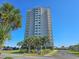 Stunning high-rise condo building with ocean views from private balconies, beautifully landscaped with vibrant palm trees and lush green grass at 9820 Queensway Blvd. # 1603, Myrtle Beach, SC 29572