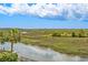Tranquil view of the waterfront backyard, with lush greenery, a dock, and marsh views under a partly cloudy sky at 172 Colony Point Dr., Georgetown, SC 29440