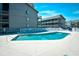 Community pool with lounge chairs surrounded by condos under a bright blue sunny sky at 9621 Shore Dr. # F-117, Myrtle Beach, SC 29572