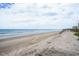 Expansive sandy beach with gentle waves, a stairway and distant buildings under a cloudy sky at 6000 N Ocean Blvd. # 133, North Myrtle Beach, SC 29582