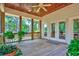 A covered porch with wood floors, ceiling fan, green plants, and an exterior view of trees and other foliage at 79 Windsor Circle Sw, Ocean Isle Beach, NC 28469