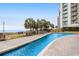 Outdoor pool with an adjacent lawn, palm trees, and ocean views on a sunny day at 2710 N Ocean Blvd. # 402, Myrtle Beach, SC 29577