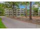 View of the condo complex surrounded by trees, landscaping, and a walking path with a bench at 415 Ocean Creek Dr. # 2245, Myrtle Beach, SC 29572