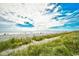 Beautiful beach view with dune grasses leading to open sand and the ocean under a partly cloudy sky at 1207 South Ocean Blvd. # 51106, Myrtle Beach, SC 29577