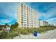 Exterior view of a tall condo building near the dunes with a partly cloudy sky at 1207 South Ocean Blvd. # 51106, Myrtle Beach, SC 29577