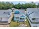 Aerial view of a light blue beach home with a covered porch, landscaping, and white fencing at 1961 Indigo Cove Ln, Calabash, NC 28467