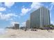 Beautiful beachfront view of a modern, high-rise condo building under a blue sky with white clouds at 201 S Ocean Blvd. # 1112, Myrtle Beach, SC 29577