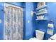 Bright blue bathroom featuring a floral shower curtain and white shelving with towels and baskets at 6813 Porcher Dr. # 21, Myrtle Beach, SC 29572